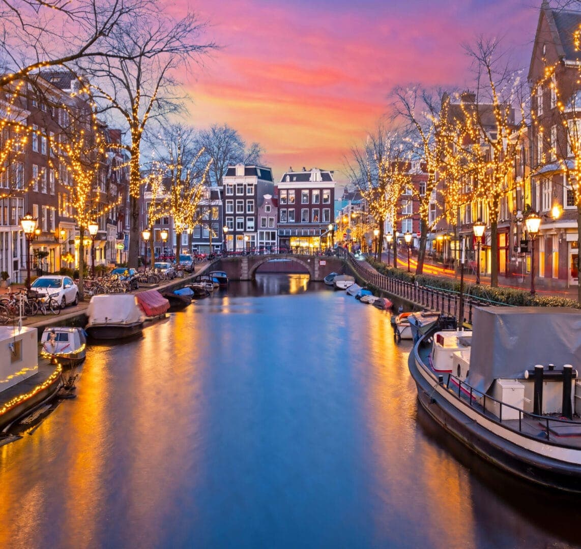 An Amsterdam canal at dusk with Christmas lights on the bridges.
