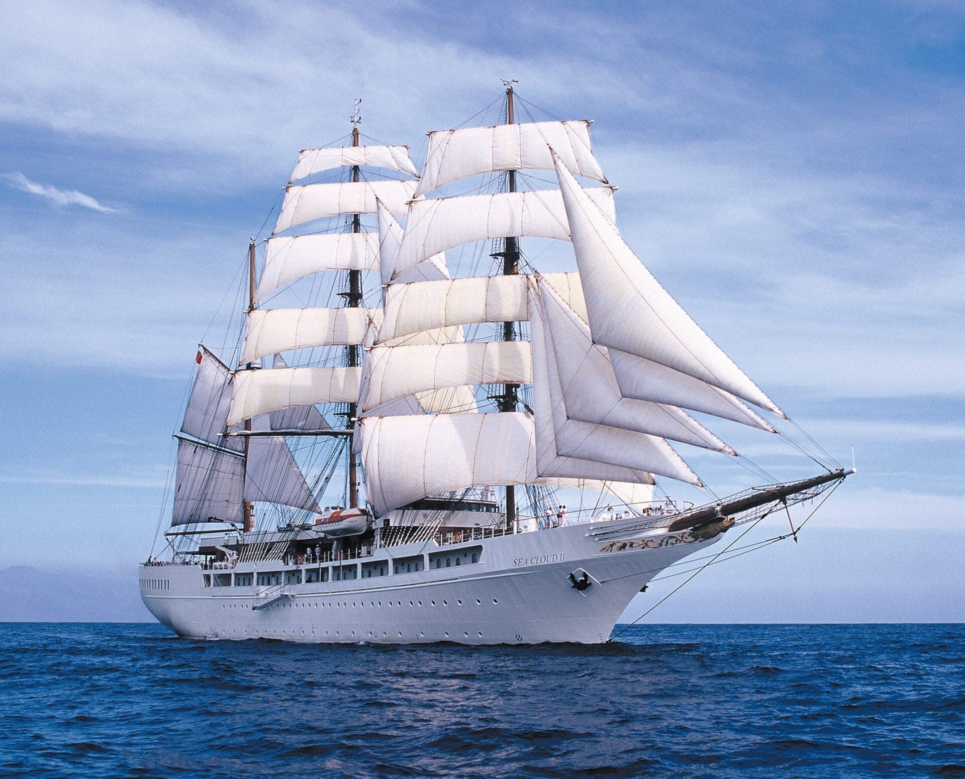 SEA CLOUD II seen from the bow quarter, sails filled, on a calm blue sea.