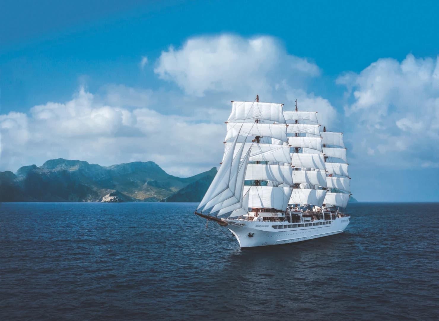 SEA CLOUD SPIRIT under full sail off a mountainous coast, clouds building over the land.